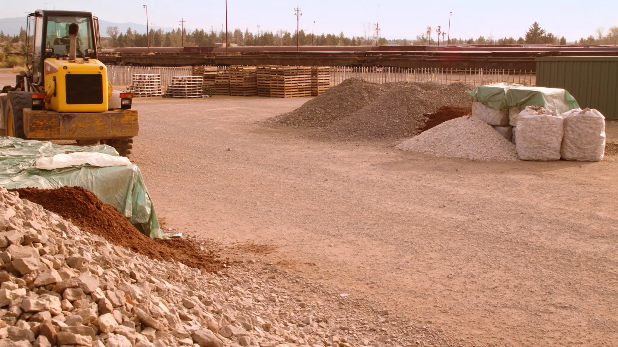 Landscape supply yard entrance with a wheel loader parked beside gravel and rock bins at golden hour