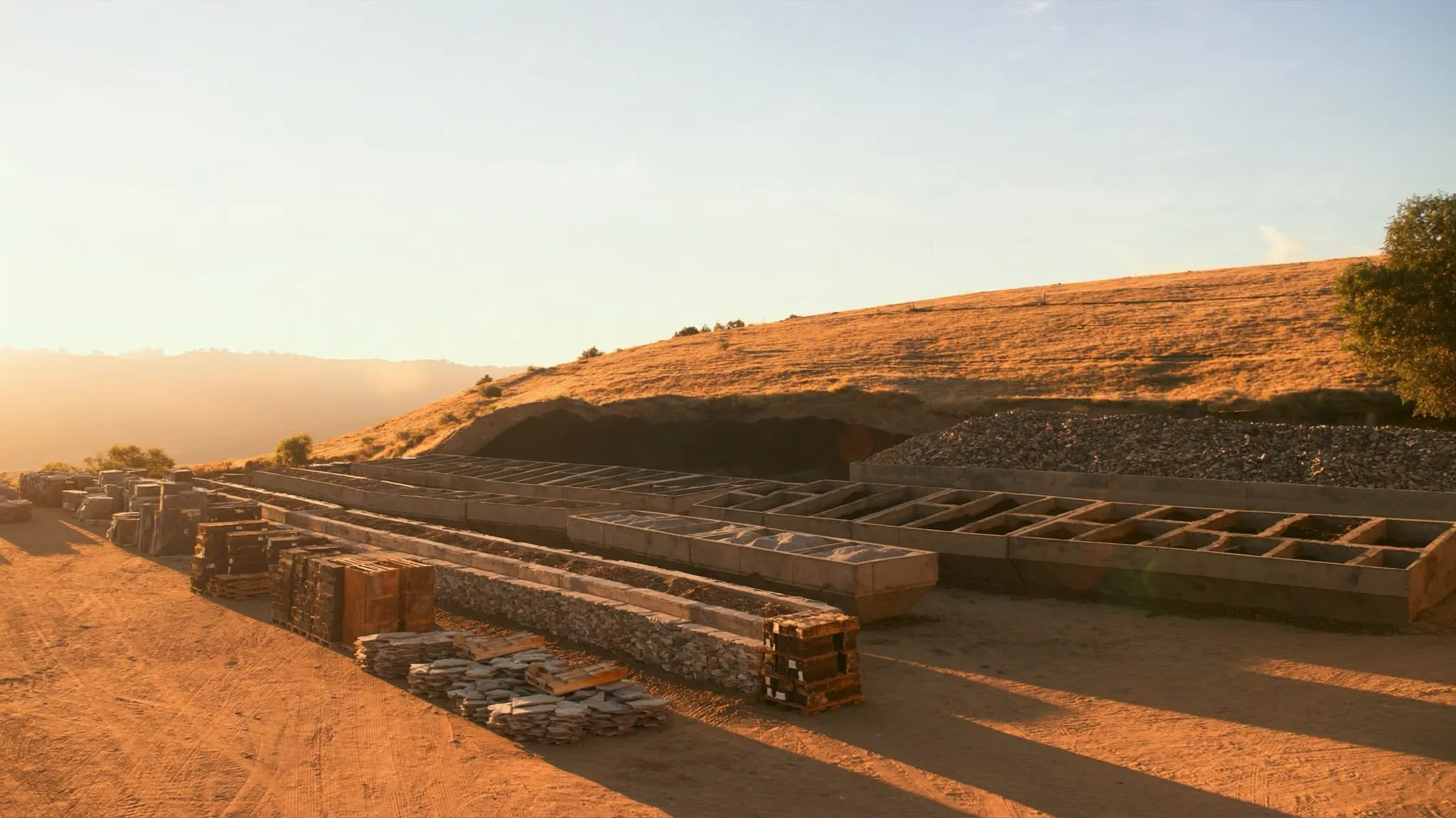 Landscape supply yard at golden hour: material bins, flagstone pallets and dry Okanagan hills